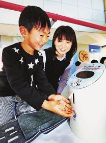 笑顔で機械から除菌液を受ける子ども（和歌山県白浜町の南紀白浜空港で）