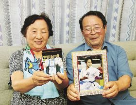 孫の清水希容選手の写真を持つ悌治さん（右）、貞子さん夫妻
