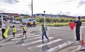 田辺署員（右）らが見守るなか、横断歩道を渡って登校する児童＝田辺市内で