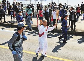 和歌山県内で始まった聖火リレーで、沿道の観客に手を振りながら走る早田卓次さん（９日、新宮市で）