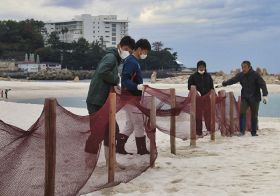 砂浜に打ち込んだくいにネットを掛けていく白浜町職員ら（２５日、和歌山県白浜町の白良浜で）