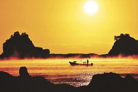 朝日に照らされ黄金色になった海霧の中を進む漁船（２９日午前６時５４分、和歌山県串本町田原で）
