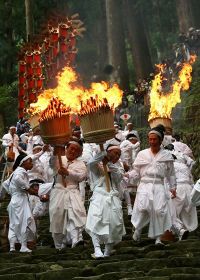 燃え盛る大たいまつを持って参道を歩く白装束の男性たち（１４日、和歌山県那智勝浦町で）