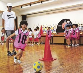 松尾直人さん（左）に教わってボールを蹴りながら走る園児＝２１日、和歌山県みなべ町西本庄で