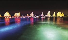 ライトに照らされ鮮やかな色に染まった水面と橋杭岩（２日、和歌山県串本町くじの川で）