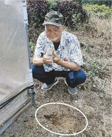 「発見現場」となった自身の農地で石斧を持つ中野文治さん。白円の辺りで見つけた＝２３日、和歌山県田辺市中辺路町栗栖川で