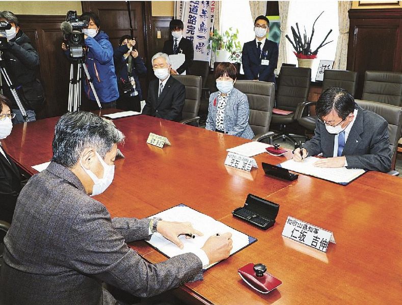 「自宅療養」に備えた協定調印式で、署名する和歌山県の仁坂吉伸知事（左）と県医師会の平石英三会長（右）＝１７日、和歌山県庁で
