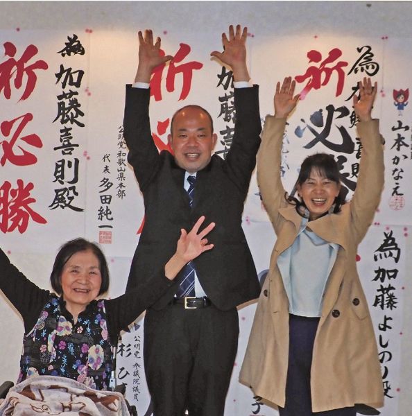 初当選を決め、万歳で喜ぶ加藤喜則さん（中央）。右は妻の由紀さん、左は母の秀子さん＝２５日午後１１時４０分ごろ、和歌山県田辺市宝来町で