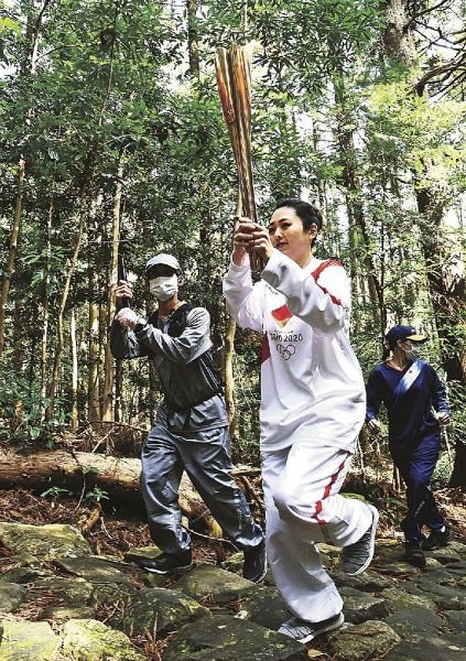 トーチを掲げ世界遺産の熊野古道大門坂を登るランナー（９日、和歌山県那智勝浦町で）