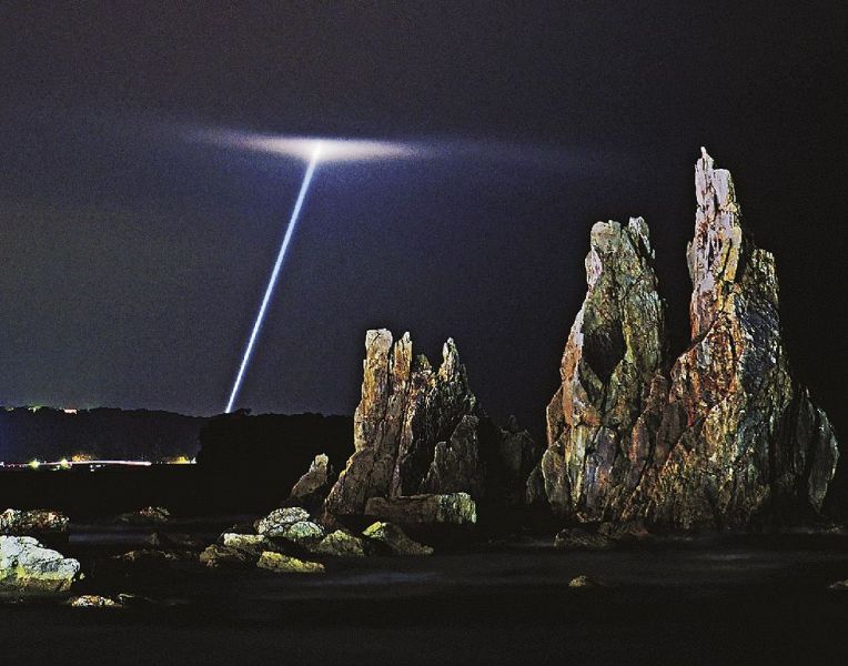 橋杭岩の背後に浮かび上がったサーチライトの光（１２日午後６時３６分、和歌山県串本町くじの川で）＝長時間露光