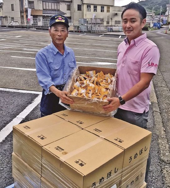 梅の郷救助隊の尾﨑剛通隊長（左）に梅干しを渡すウメタの泰地雄也業務企画室長＝９日、和歌山県みなべ町山内で