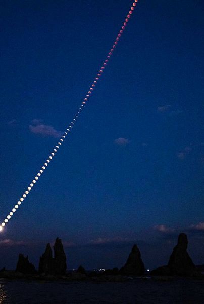 串本町にある国の名勝・天然記念物「橋杭岩」の上で皆既月食へと変化した月（８日午後５時２３分から３分間隔で撮影した月を合成）