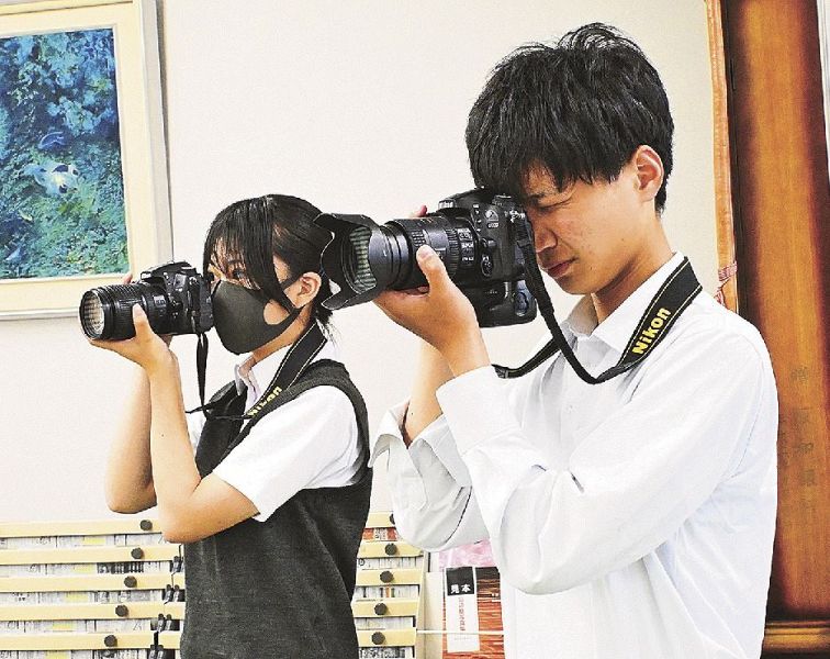 一眼レフカメラで、勤務中の社員を撮影する尾花誠矢さん（右）と加賀登一香さん＝和歌山県田辺市秋津町で